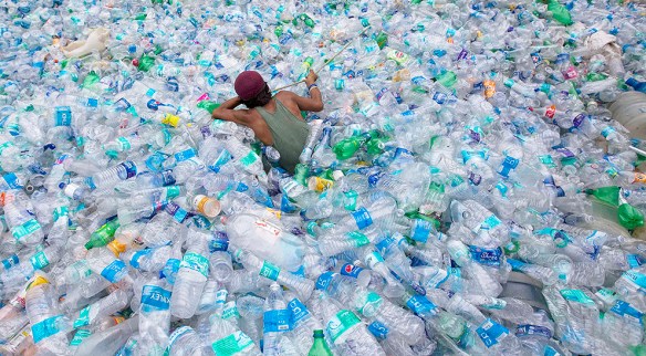 A worker uses a rope to move through a pile of empty plastic bottles at a recycling workshop in Mumbai